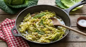 Padella con verza stufata in olio con aglio su tavolo rustico, con cucchiaio di legno e foglie di verza accanto
